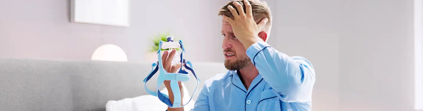 Man in bed frustrated with his CPAP mask.